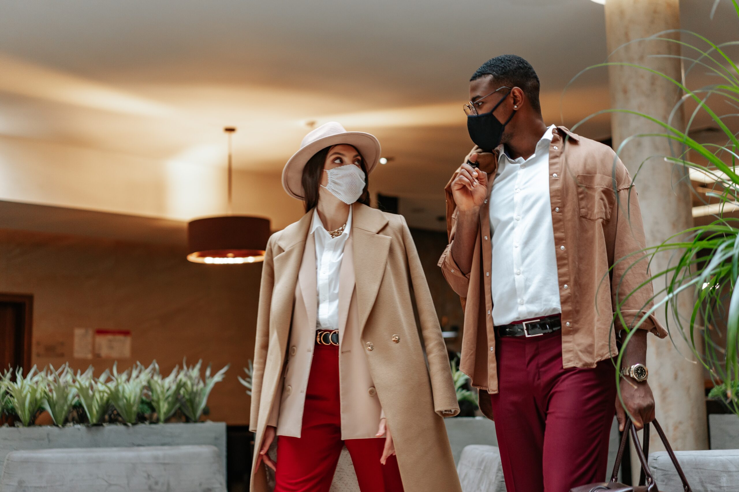 man and woman in airport going on a business trip. They are both waring red pants and khaki coats and carry their luggage. 10 Tips To Help You Reduce Costs And Increase Efficiency.