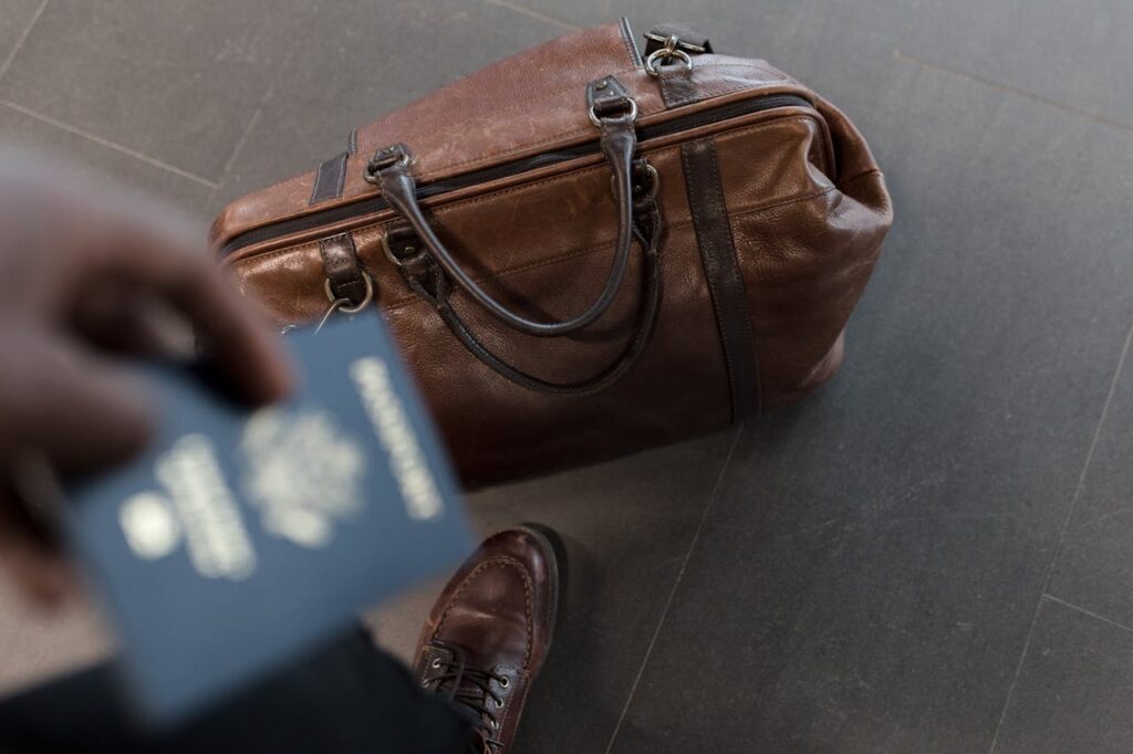 A man holding a passport while his bag is beside him on the floor.