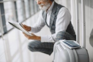 A white-bearded man with the newspaper, sitting crouched near the luggage.