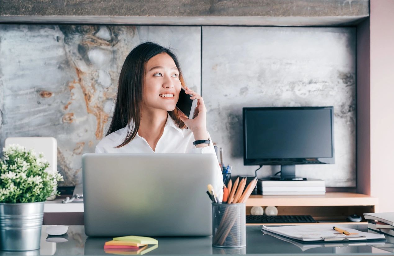 woman sitting at a desk on her phone with a laptop in front of her